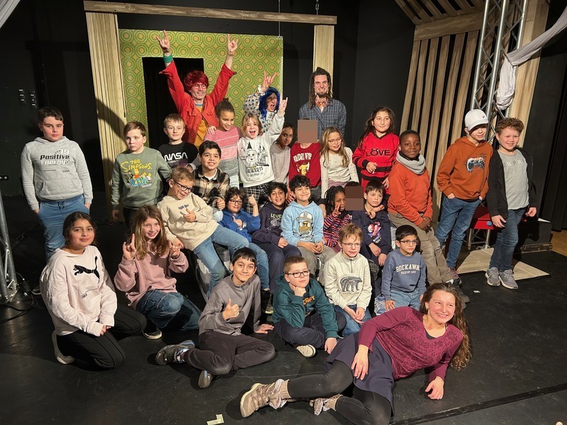 Das Bild zeigt: Alle Kinder der Klassen E bis 4 sind mit den 3 Schauspieler:innen und der Dolmetscherin auf der Bühne.